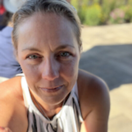A middle aged woman wearing a white tank top sweater looks at the camera, hair pulled back.